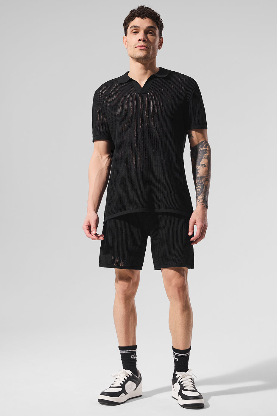 Front angle of black V-neck polo shirt styled with white shorts on golf green