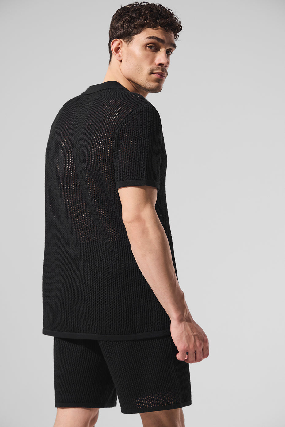 Front angle of black V-neck polo shirt styled with white shorts on golf green