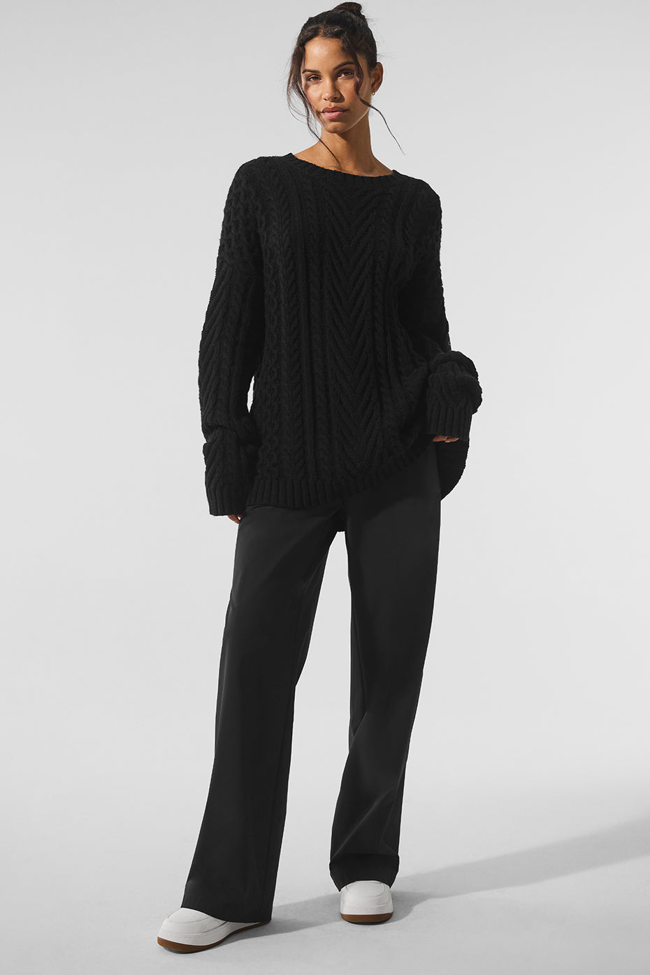 Front view of a black cable knit crew neck sweater on a model, showcasing its textured pattern
