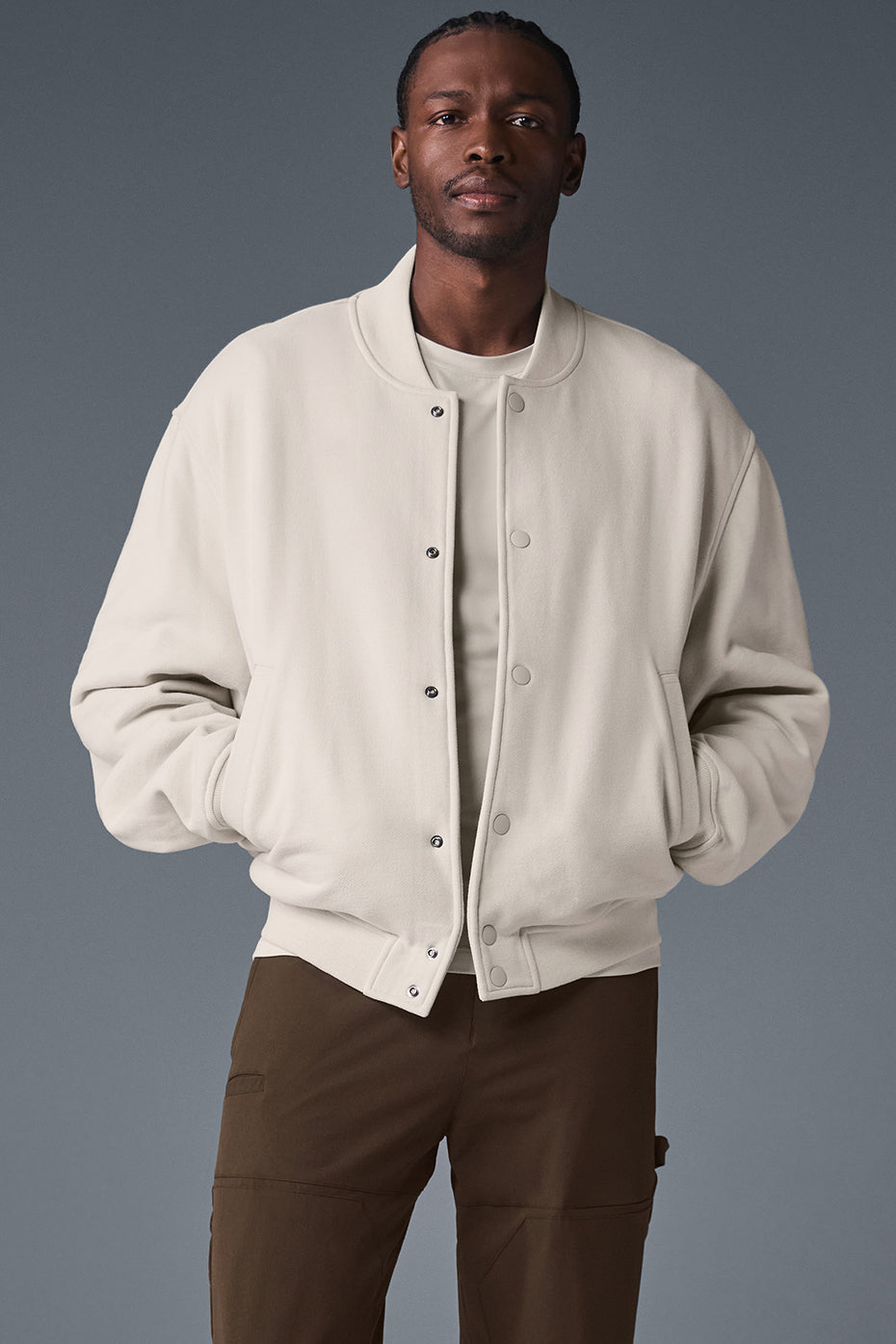 Front view of the men's varsity jacket in bone with drop shoulders and button closure