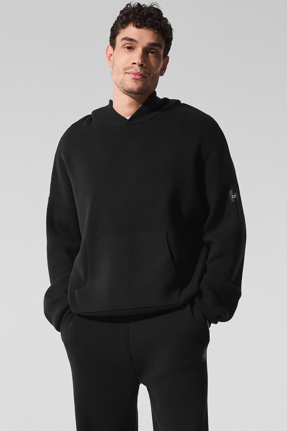 Front view of the black hooded sweater with knitted texture and kangaroo pocket