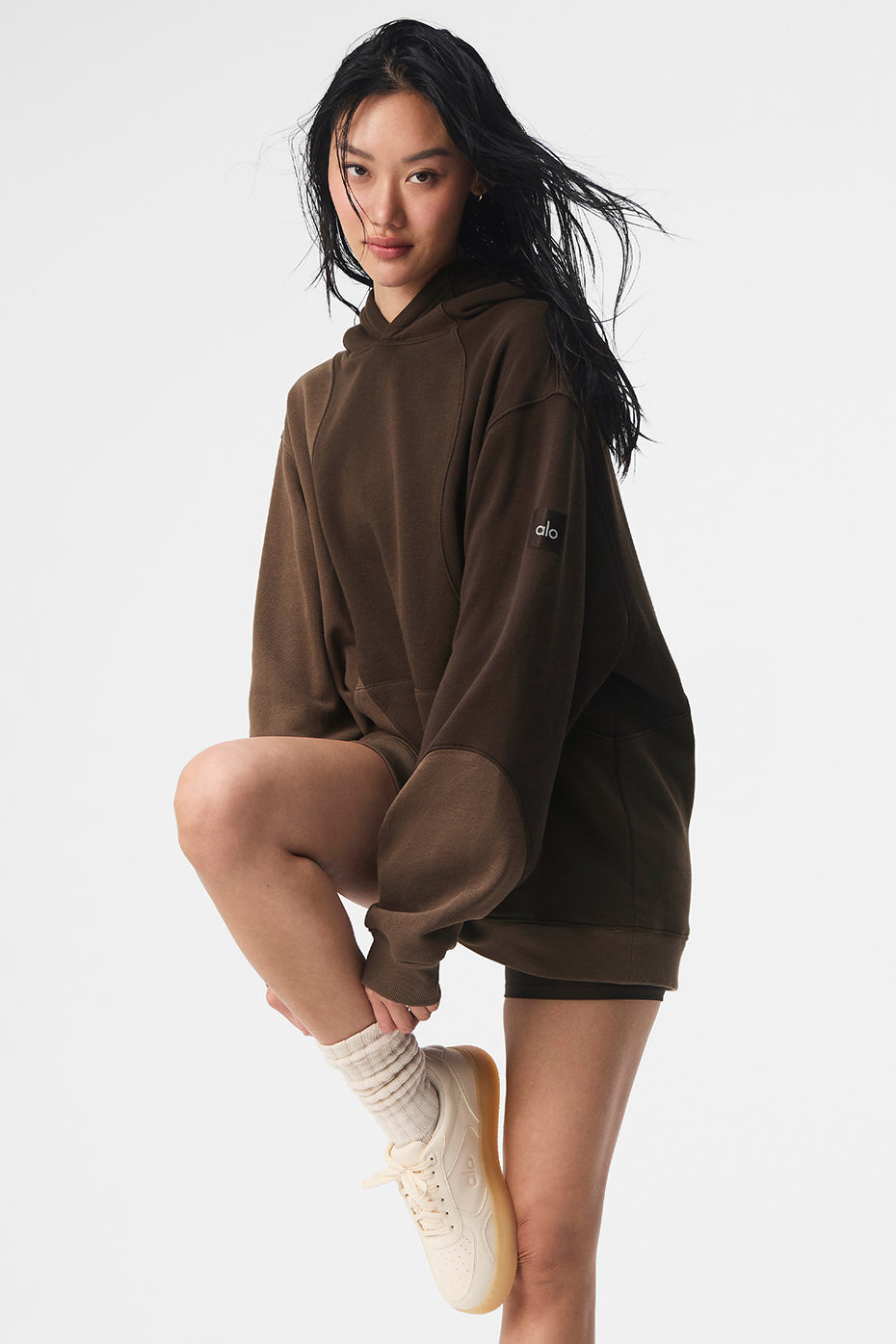 Male model wearing mens oversized hoodie in espresso shade, walking on urban rooftop.