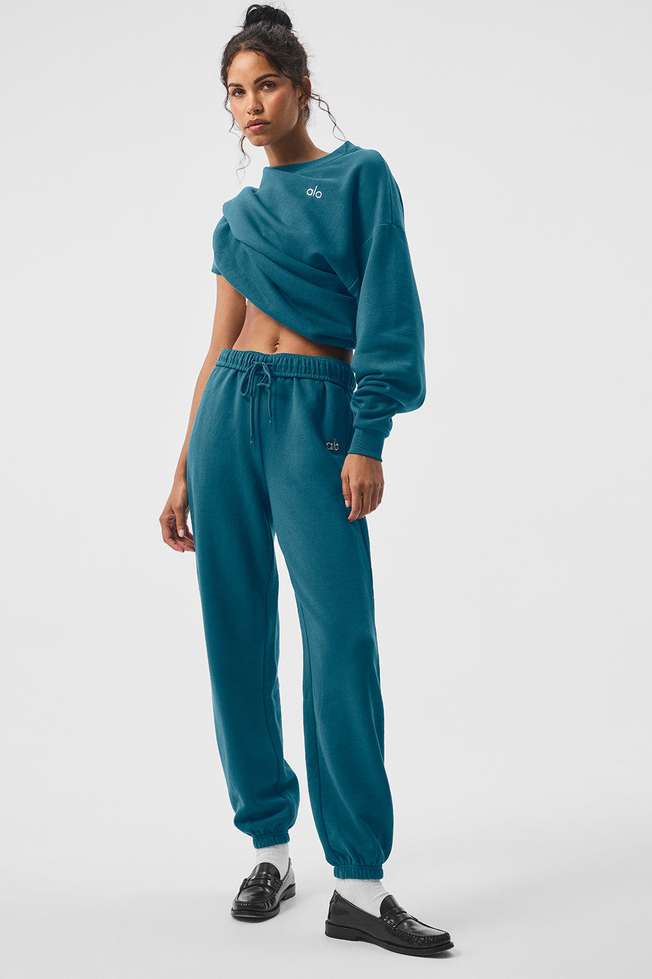 Tall man wearing oceanic teal sweatpants, leaning against a brick wall
