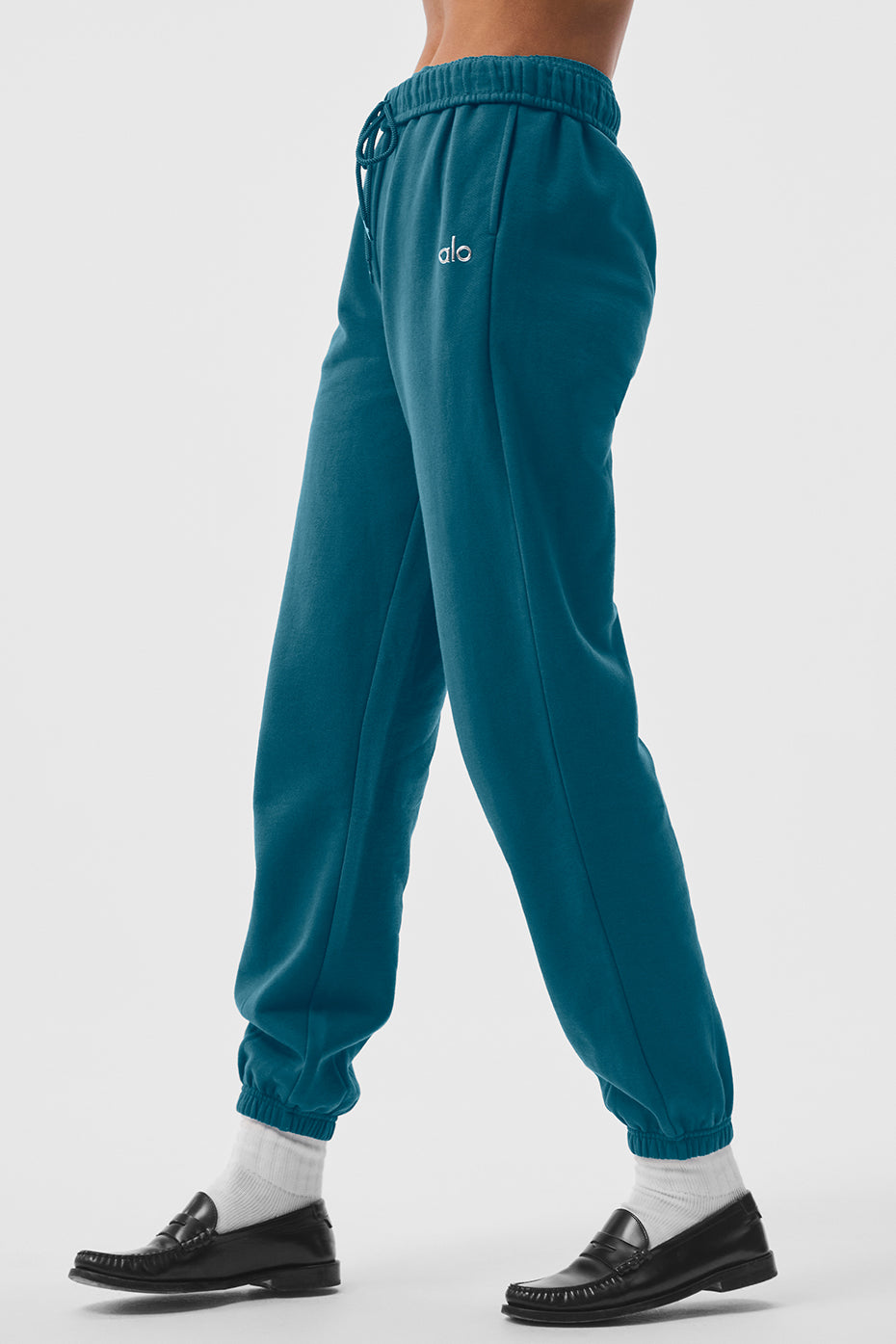 Tall man wearing oceanic teal sweatpants, leaning against a brick wall