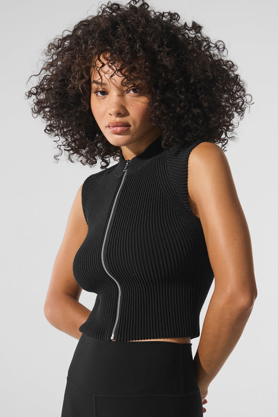 Side angle showing structured fit of black zip-up tank top, matched with wide-leg trousers