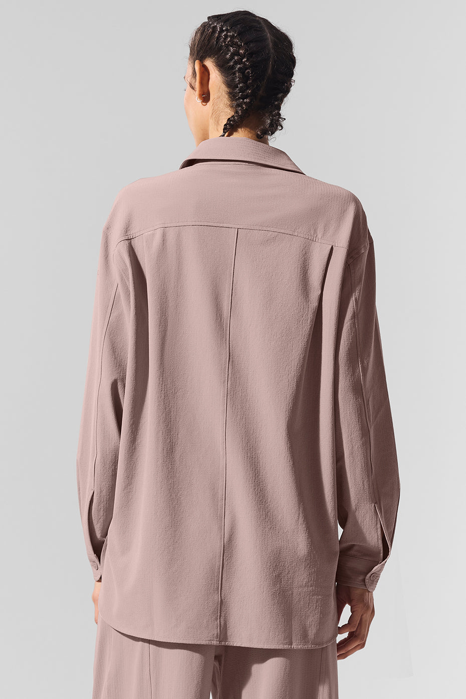 Woman in a taupe oversized button down shirt with front pockets, posing outdoors.