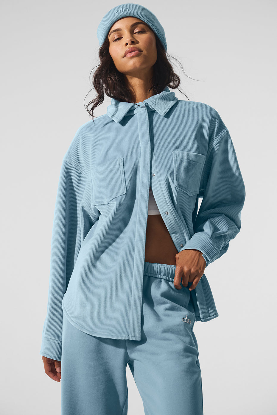 Model wearing denim shacket open over layered knit top in autumn foliage setting