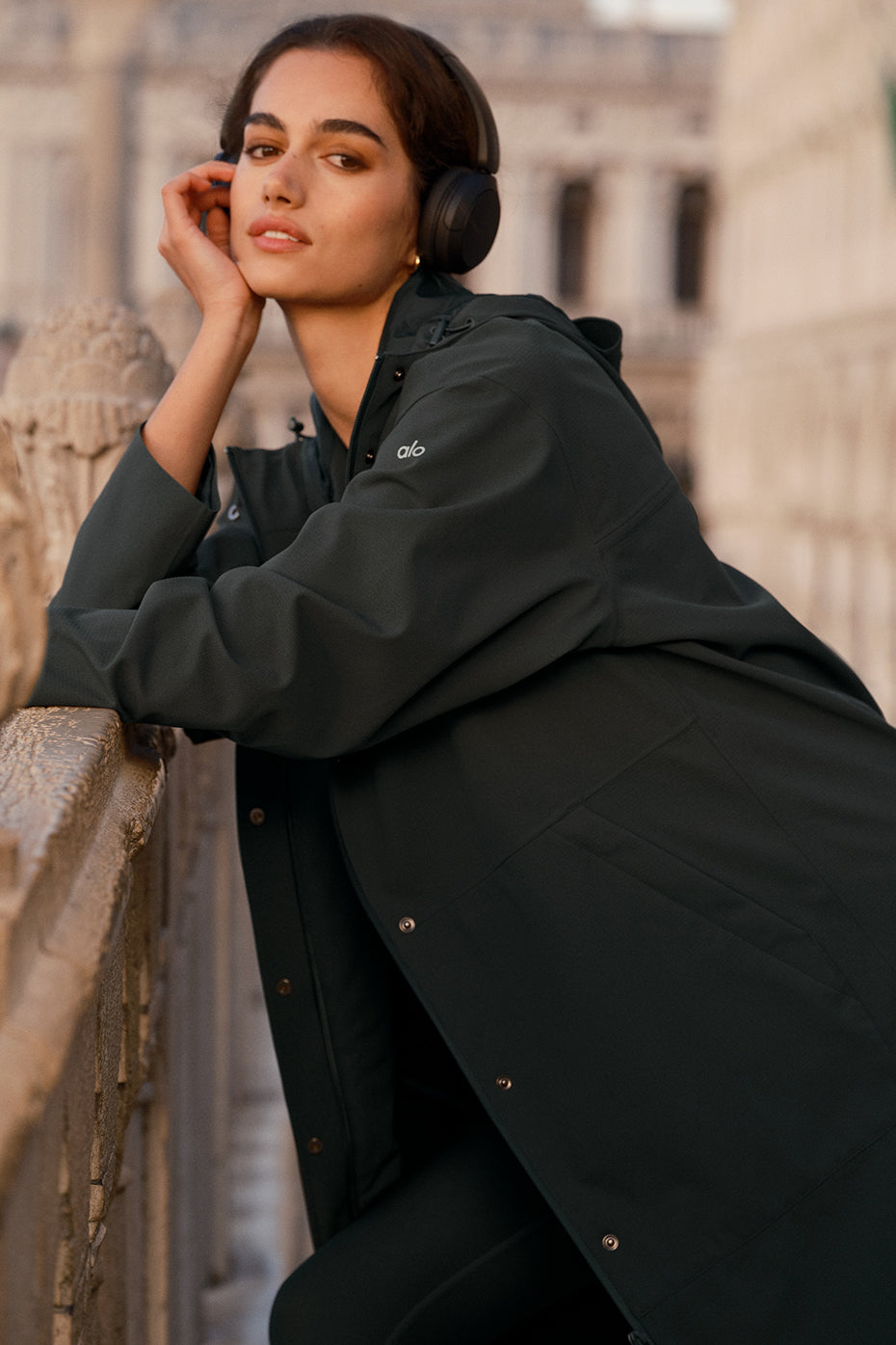 Waterproof long coat worn in urban rain setting, hood adjusted