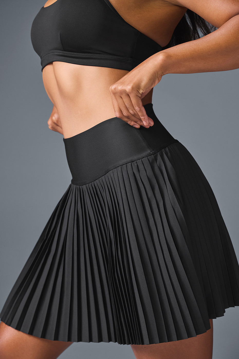Woman playing tennis in a stylish pleated black skirt.