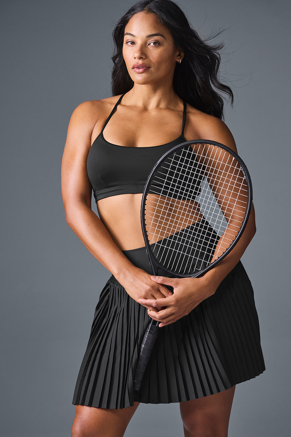 Woman playing tennis in a stylish pleated black skirt.
