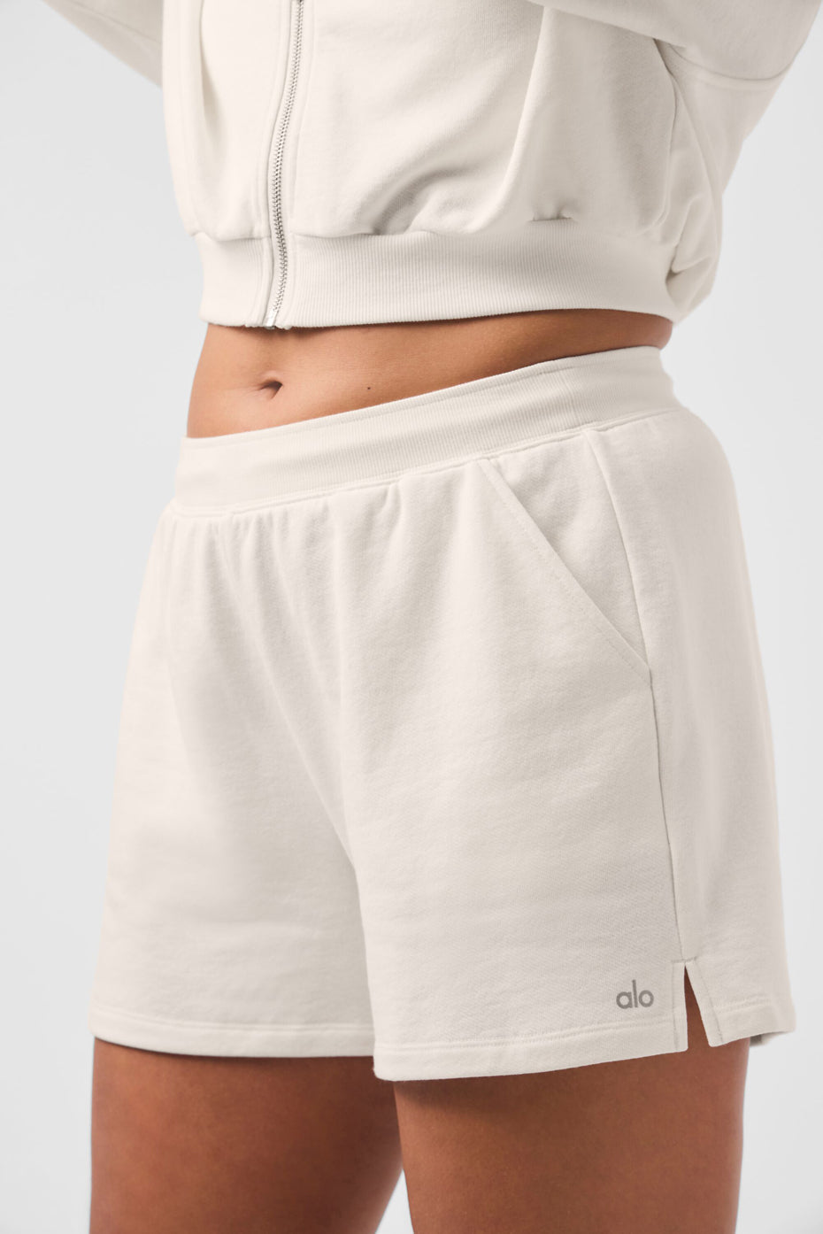 Model wearing high rise sweat shorts, styled with a zip-up hoodie.