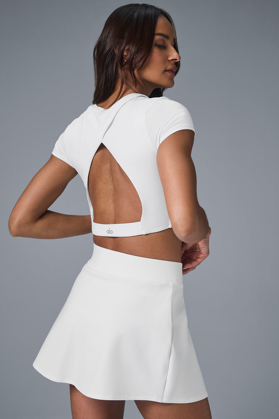 Model wearing the white tennis skirt on the court, highlighting its flowy design.