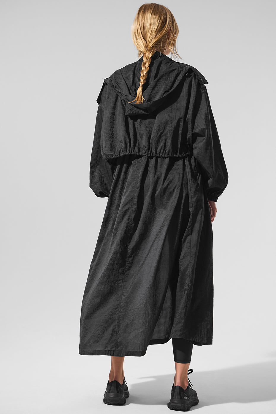 Front view of black trench coat styled with activewear cover-up under soft lighting