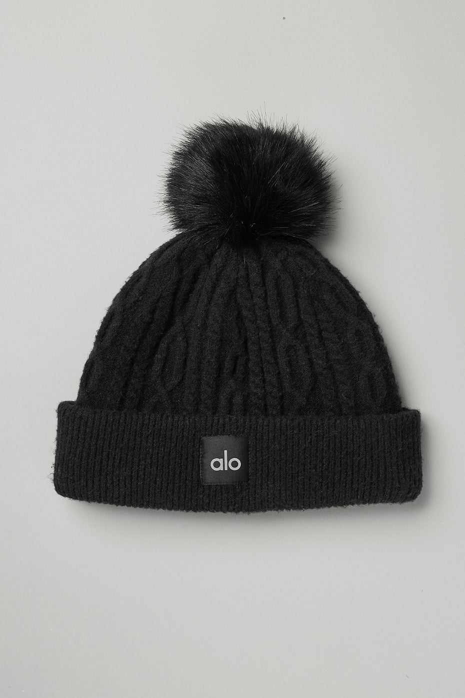 Close-up of black cable knit beanie with faux fur pom.