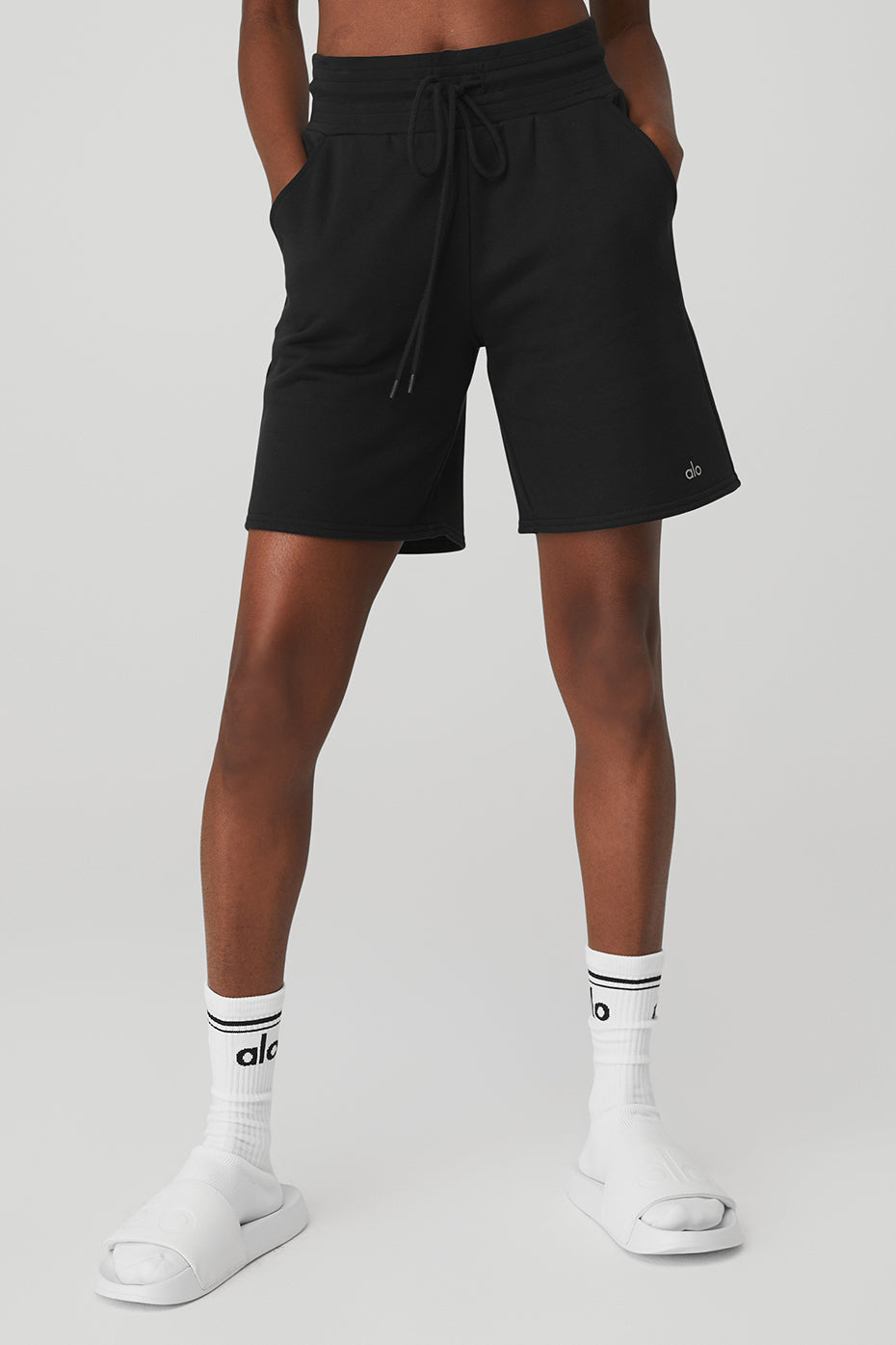 Side view of black high-waist shorts styled with slides and bra top outdoors